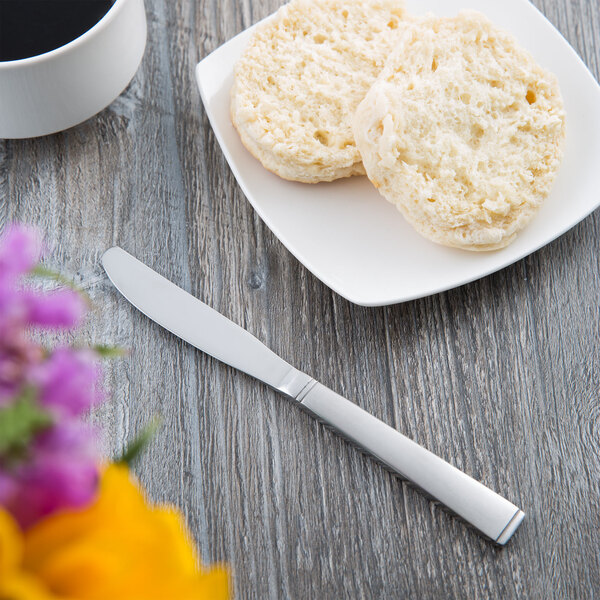 A knife next to a plate of biscuits and a cup of coffee on a table.