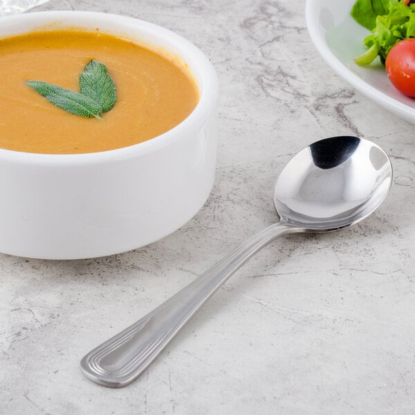 A bowl of soup with a Libbey stainless steel bouillon spoon next to it.