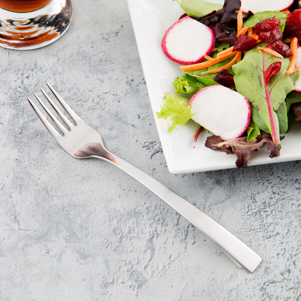 A Libbey stainless steel salad fork on a plate of salad with a glass of liquid.