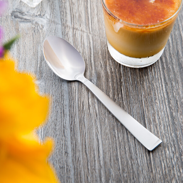 A Libbey stainless steel teaspoon on a table next to a glass of liquid.