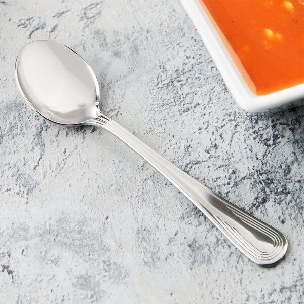 A Libbey stainless steel round bowl soup spoon next to a bowl of soup.