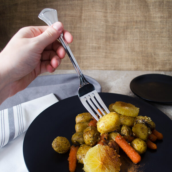 A hand holding a World Tableware Resplendence dinner fork over a plate of potatoes and carrots.