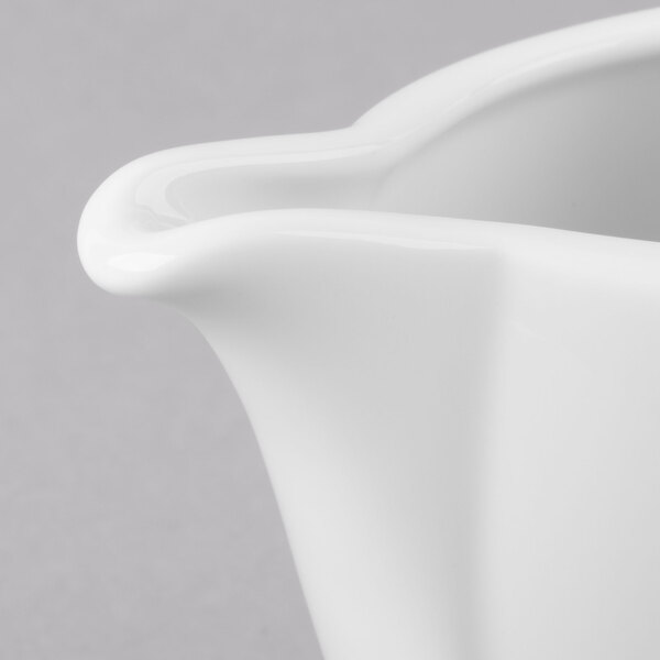 A close-up of a Schonwald white porcelain creamer with a handle.
