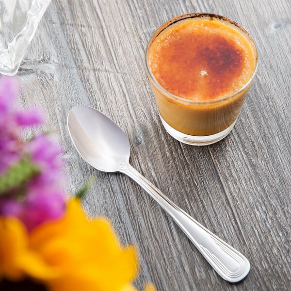 A Libbey stainless steel teaspoon in a glass of orange liquid on a table.