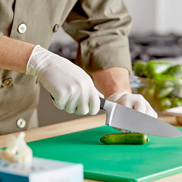 A person wearing Noble Products white powdered latex gloves using a knife to cut a cucumber on a counter in a professional kitchen.