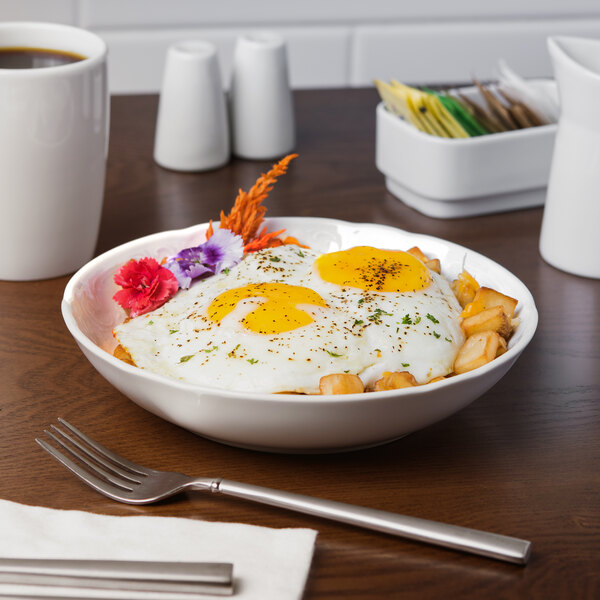 A Schonwald white porcelain bowl filled with food with a fork and a cup of coffee on a table.