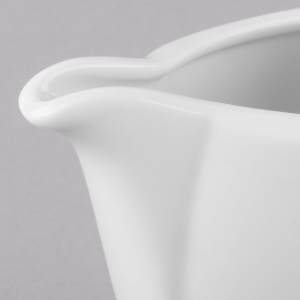 A close-up of a Schonwald Avanti Gusto white porcelain creamer with a handle.