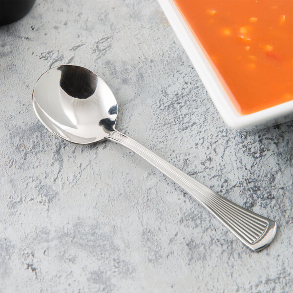 A Libbey stainless steel bouillon spoon next to a bowl of soup.