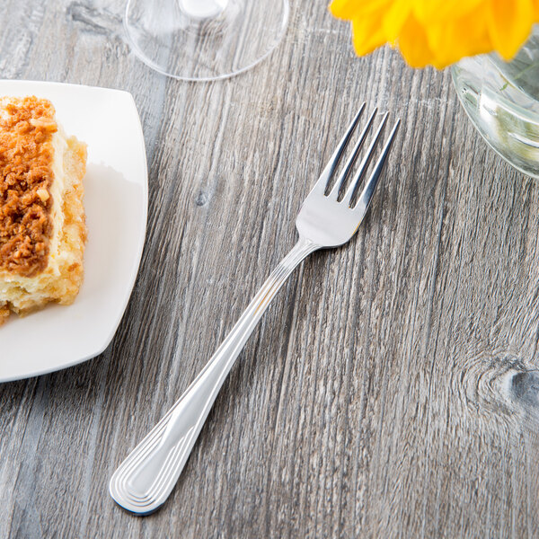 A Libbey stainless steel utility fork on a plate with a piece of cake.