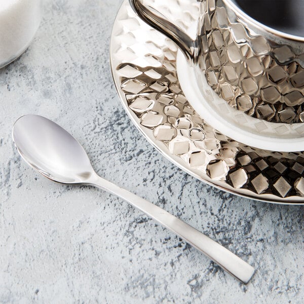 A Libbey stainless steel demitasse spoon on a white plate with a silver cup and saucer.