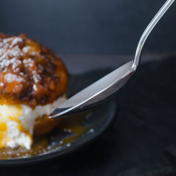 A World Tableware Resplendence stainless steel dessert spoon on a plate with a piece of cake.