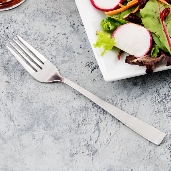 A Libbey stainless steel salad fork next to a plate of salad.