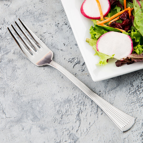 A Libbey stainless steel salad fork next to a plate of salad.