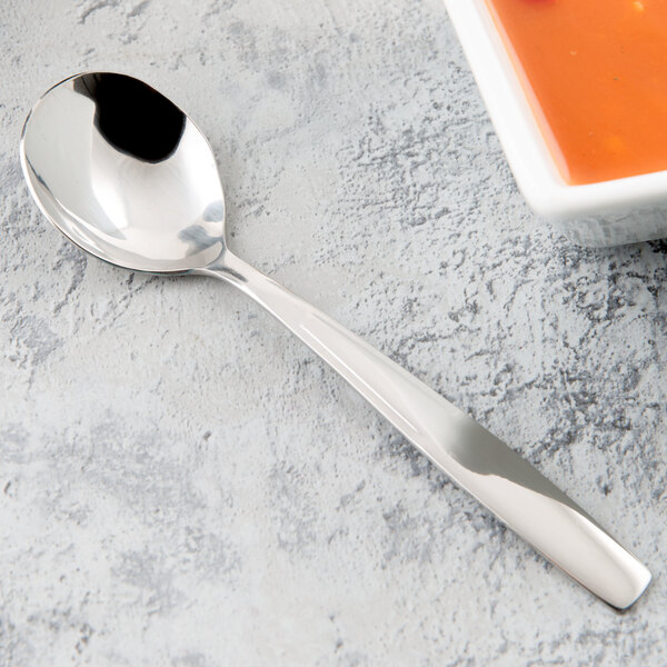 A Libbey stainless steel bouillon spoon next to a bowl of soup.