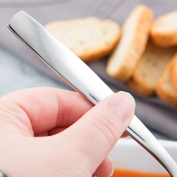 A hand holding a Libbey stainless steel bouillon spoon over a bowl of soup.