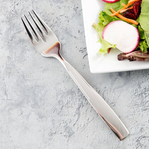 A Libbey stainless steel salad fork next to a plate of salad.