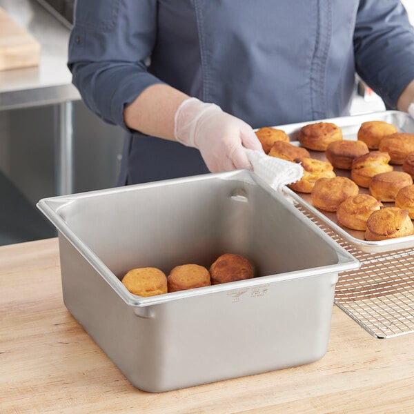 A woman holding a Vollrath stainless steel steam table pan full of pastries.