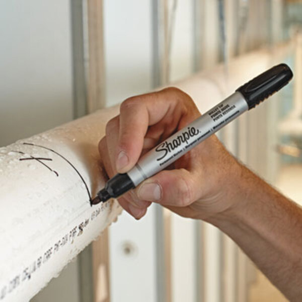 A hand writing "Sharpie Pro" on a pipe with a black Sharpie marker.