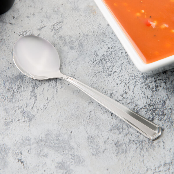 A Libbey stainless steel bouillon spoon next to a bowl of soup.