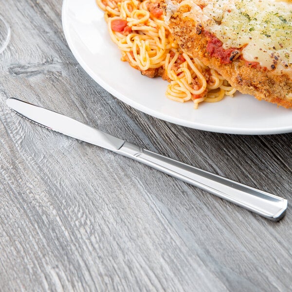 A Libbey stainless steel dinner knife on a table with a plate of food.