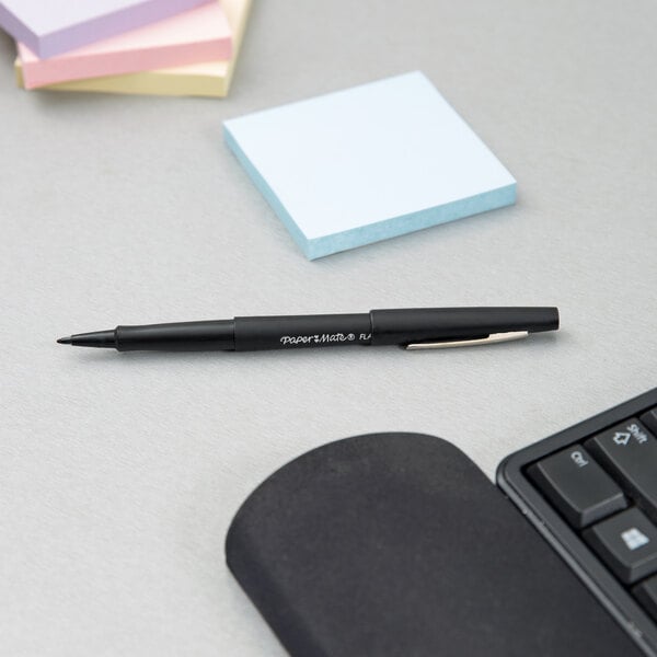 A Paper Mate black stick pen next to sticky notes on a table.