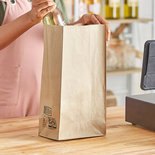 A woman opening a brown paper bag with a bottle of wine inside.