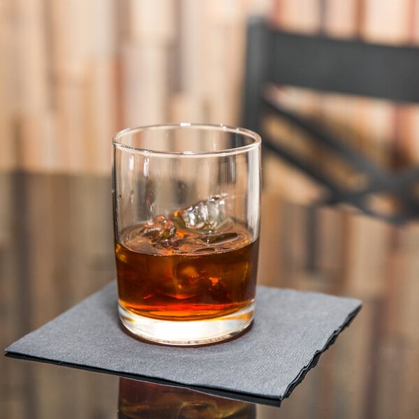 A Libbey room tumbler with a drink and ice on a napkin.