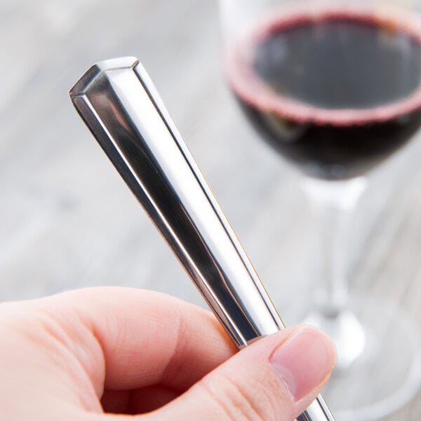 A hand holding a Libbey stainless steel dinner fork next to a glass of wine.