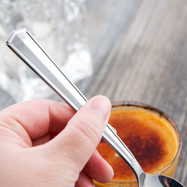 A hand holding a Libbey stainless steel teaspoon over a cup of liquid.