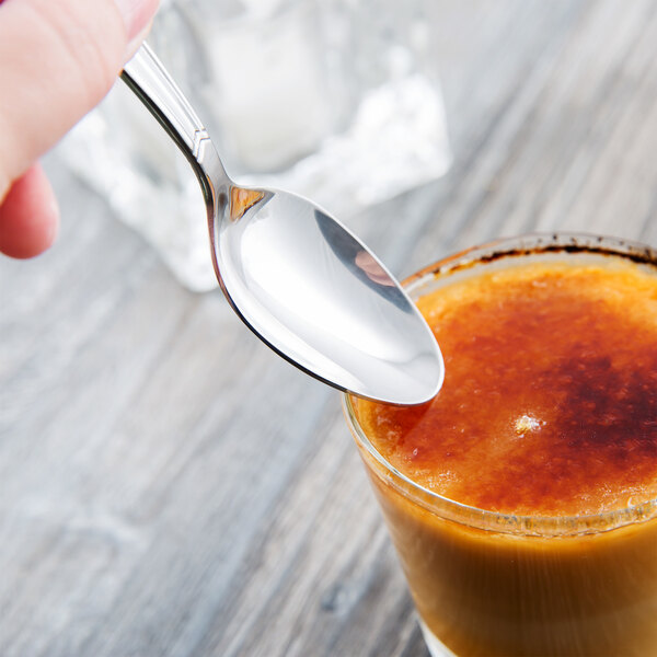 A hand holding a Libbey Vermont stainless steel teaspoon over a glass of liquid.