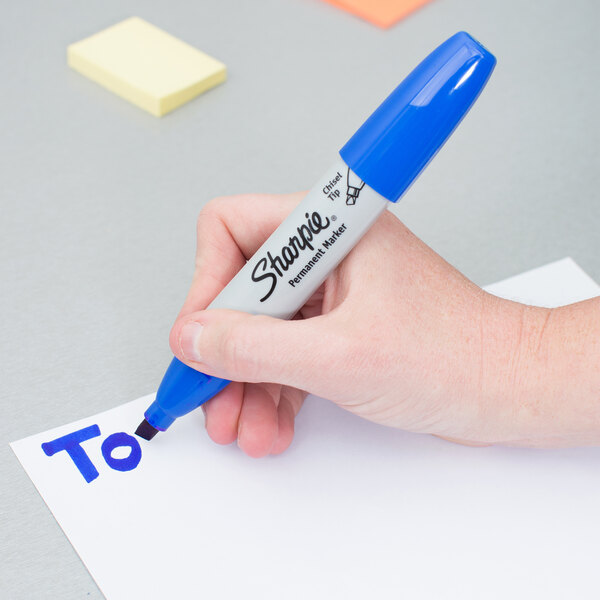 A hand holding a blue Sharpie marker over a piece of paper.