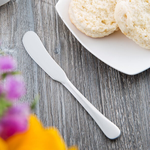A white plate with butter and a biscuit next to a Reserve by Libbey stainless steel butter spreader.