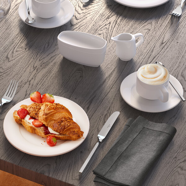 A white porcelain sugar bowl with a lid, placed on a wooden table among other breakfast items.