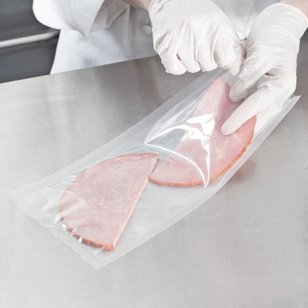 A person wearing gloves places a piece of ham in a VacPak-It plastic bag.