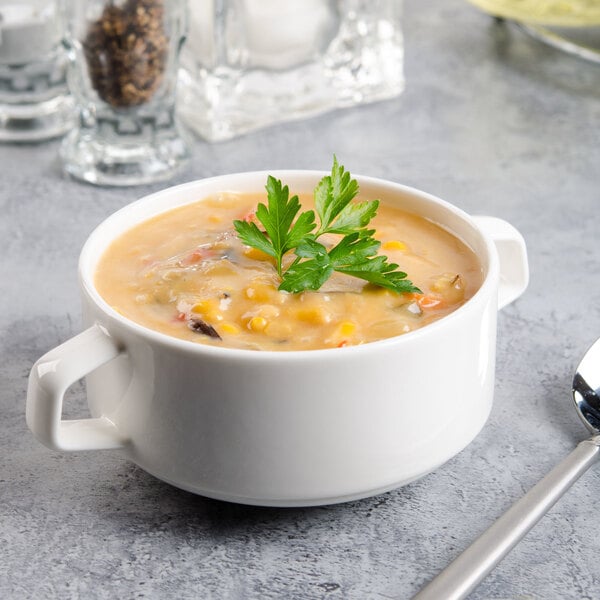 A Villeroy & Boch white porcelain stackable soup cup with a bowl of soup and a leafy green garnish.