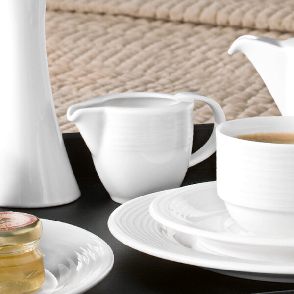 A close-up of a Villeroy & Boch white porcelain creamer on a tray with a white tea set and a cup of tea.