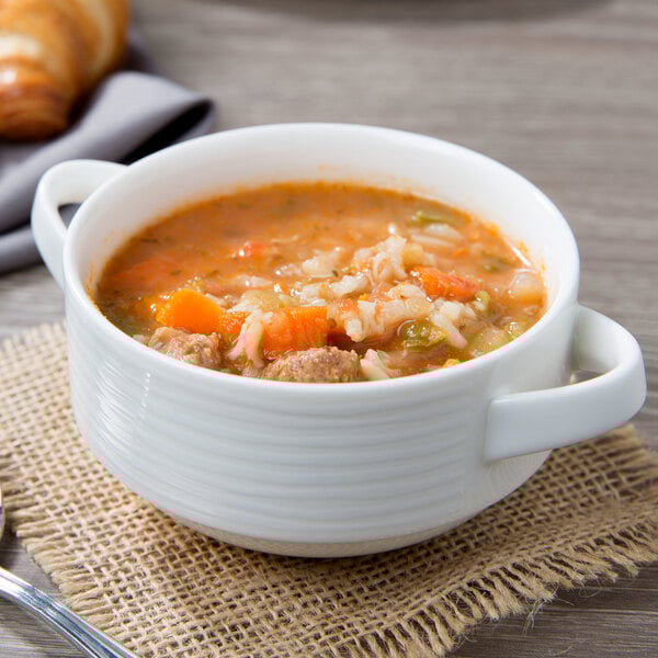 A stackable white porcelain soup cup filled with soup and vegetables.