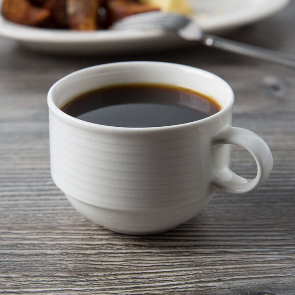 A Villeroy & Boch white porcelain stackable cup of coffee on a table next to a plate of food.
