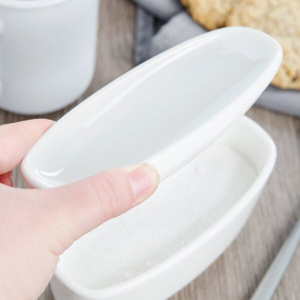 A person holding a Villeroy & Boch white porcelain sugar bowl cover over a white bowl.