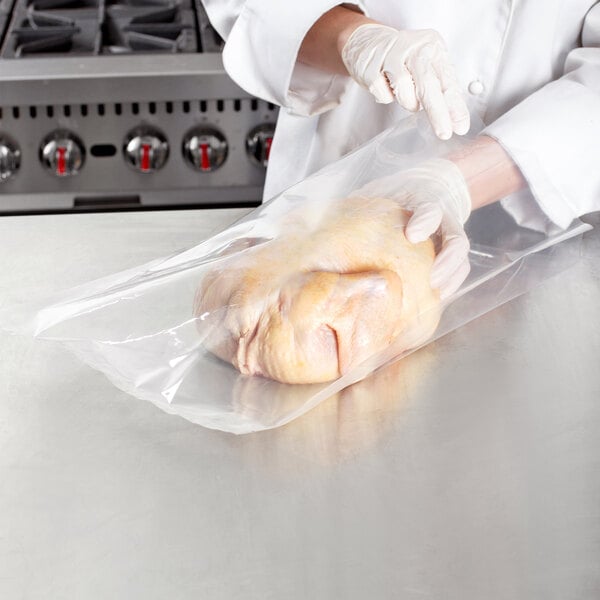 Gloved hands placing raw chicken inside bag for vacuum sealing