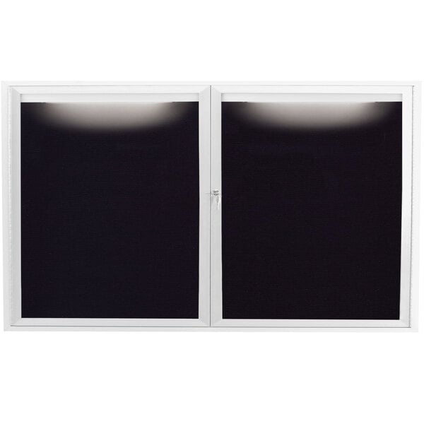 A white aluminum message center with two black doors and a black letter board inside a window with a light.