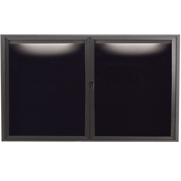 A black rectangular Aarco indoor message center with two glass doors and a light on it.