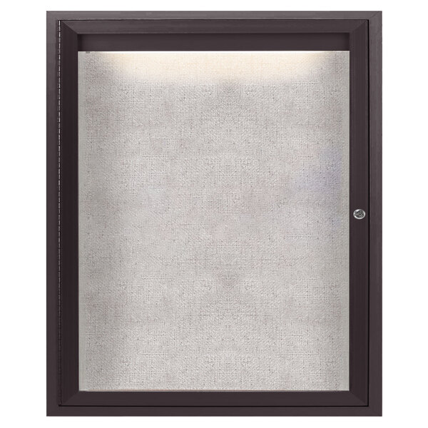 The hinged door of an Aarco bronze anodized outdoor bulletin board with a black frame.