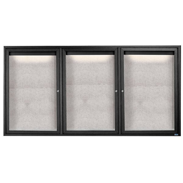 A black cabinet with three glass doors and a white rectangular board inside with a black frame.