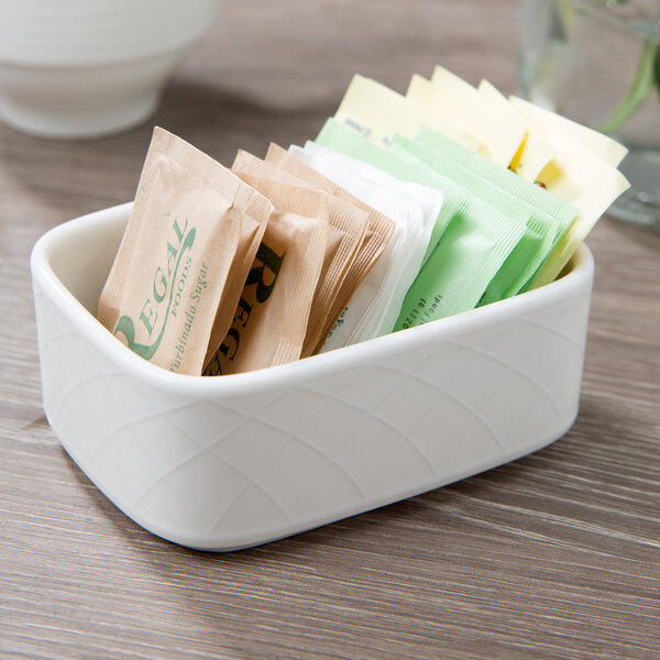 A white rectangular porcelain container with sugar packets in it.