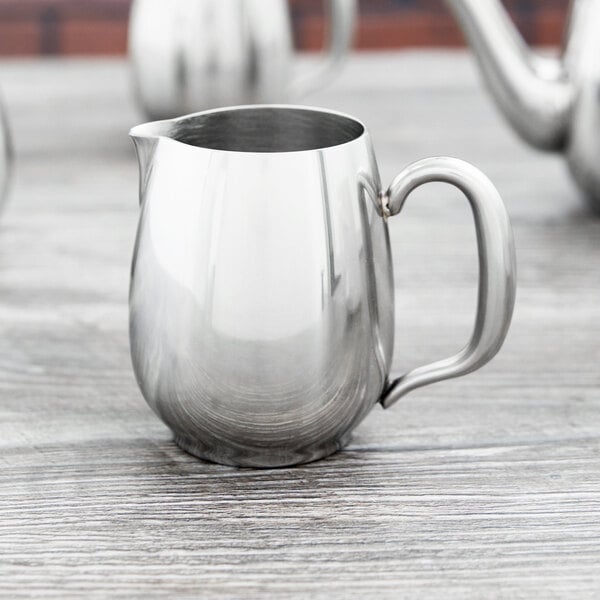 A Vollrath stainless steel open creamer with a lid and handle.