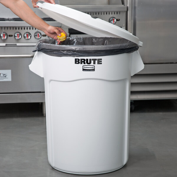 A woman putting food in a white Rubbermaid trash can with a black liner.