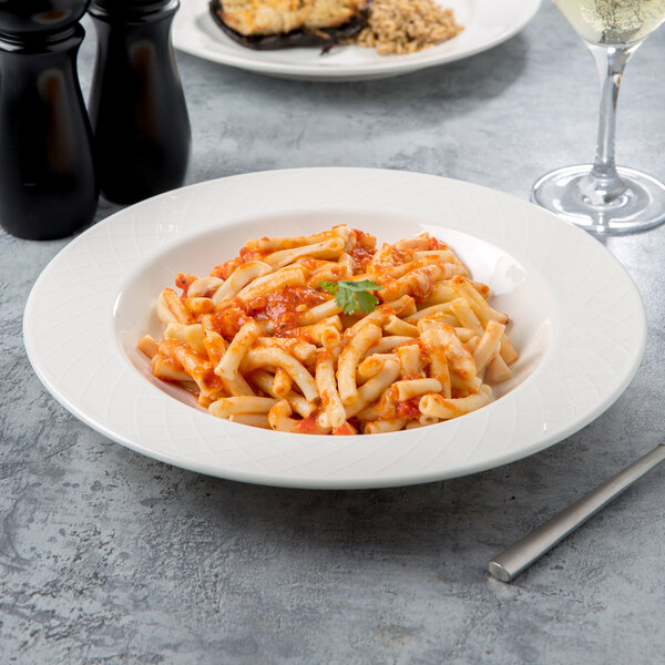 A Villeroy & Boch white porcelain rim soup bowl filled with pasta and a glass of wine on a table.