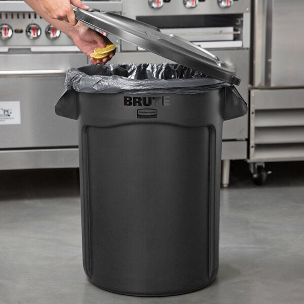 A person putting a lemon in a black Rubbermaid trash can.
