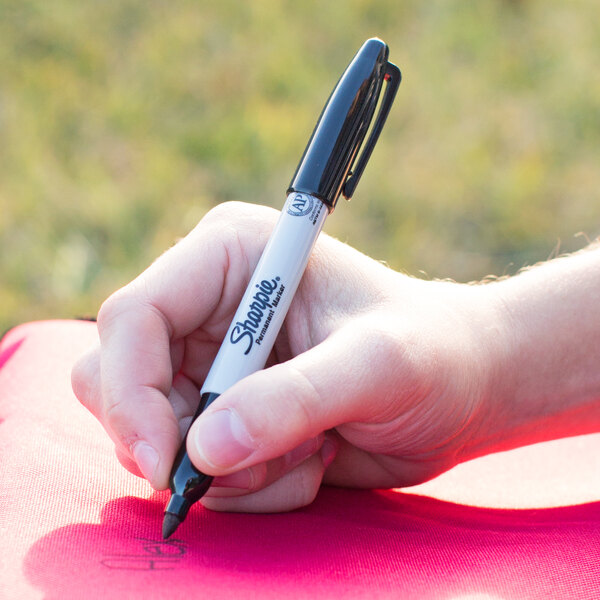 A hand using a Sharpie Extreme Black Fine Point marker to write on paper.